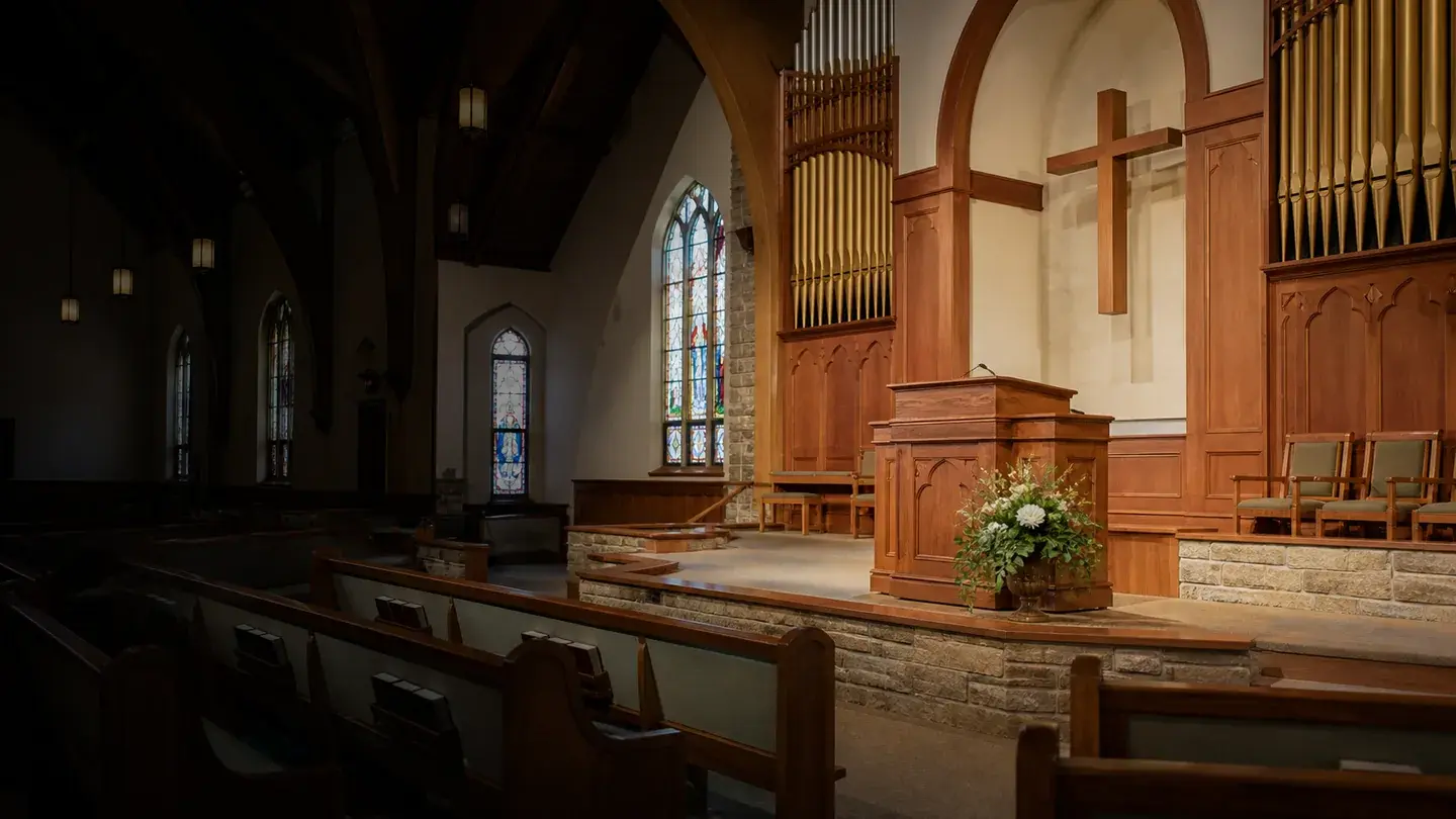 A church sanctuary with stained-glass windows, organ pipes, and a wooden pulpit.
